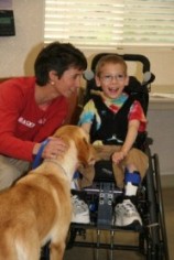 Boy in Wheelchair being greeted by a Dog while an adult dog handler looks on