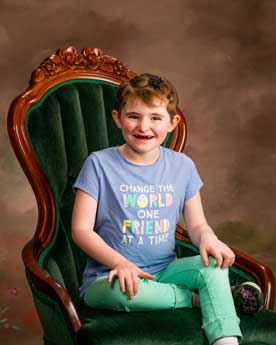 Child with Angelman Syndrome sitting in a large chair and smiling at the camera