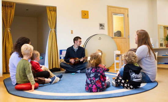 children sitting in circle while teacher plays mandolin as music therapy