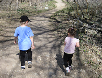Two children walking down a dirt path with trees on either side